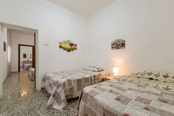 Una habitación con dos camas, una mesita y una lámpara en la pared.