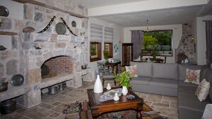 A stone fireplace with a brick surround, a wooden table with white vases and a tray, and a grey sofa with floral cushions. - Room-authentic Boutique Hotel (Fethiye)