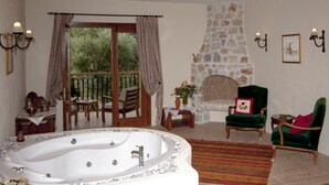 A spacious room with a large bathtub, a stone fireplace, and a cozy seating area with a green armchair and a wooden table. - Room-authentic Boutique Hotel (Fethiye)