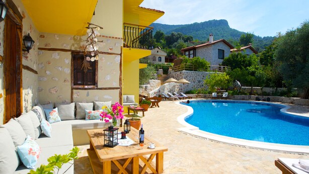 A poolside area with a wooden table, a sofa, and a view of a mountain. - Room-exclusive Boutique Hotel 4 (Fethiye)
