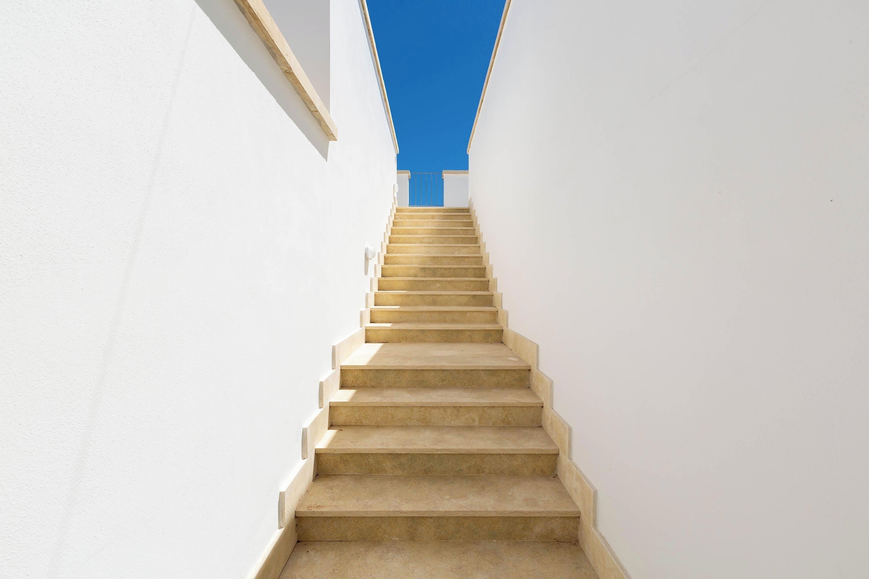 Una escalera recta color beige que sube entre paredes blancas.