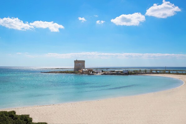 A beach with a tower structure, clear blue water, and a sandy shore.