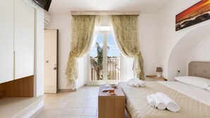 Une chambre à coucher avec un lit, une table de chevet, une fenêtre avec des rideaux, un tableau au mur et une vue sur l’extérieur.