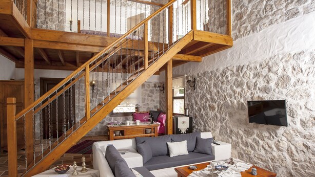 A spacious living area with a wooden staircase, a sofa set, a dining table, and a stone wall. - Room-exclusive Boutique Hotel 3 (Fethiye)
