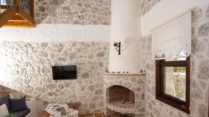 A stone-walled room with a fireplace, a flat-screen TV, and a window with a view. - Room-exclusive Boutique Hotel 3 (Fethiye)