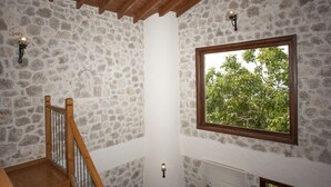 A stone-walled room with a wooden staircase, a window with a view of trees, and a wall-mounted light fixture. - Room-exclusive Boutique Hotel 3 (Fethiye)