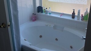 Ein Badezimmer mit einer Badewanne, einem Fenster mit geätztem Glas und Pflegeprodukten auf der Fensterbank.