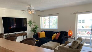 Ein Wohnzimmer mit Fernseher, Sofa, Sesseln, einem Esstisch und einem Deckenventilator.