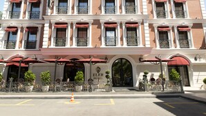 La façade d’un hôtel, ornée de nombreuses fenêtres, de stores rouges et de balcons en fer forgé décoratifs.