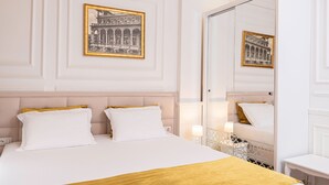 Une chambre d’hôtel avec un grand lit, une tête de lit, deux tables de chevet, un miroir et des tableaux encadrés au mur.