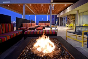 An outdoor seating area with colorful striped sofas and chairs, a central fire feature, and a covered patio with wooden ceiling and glass doors.