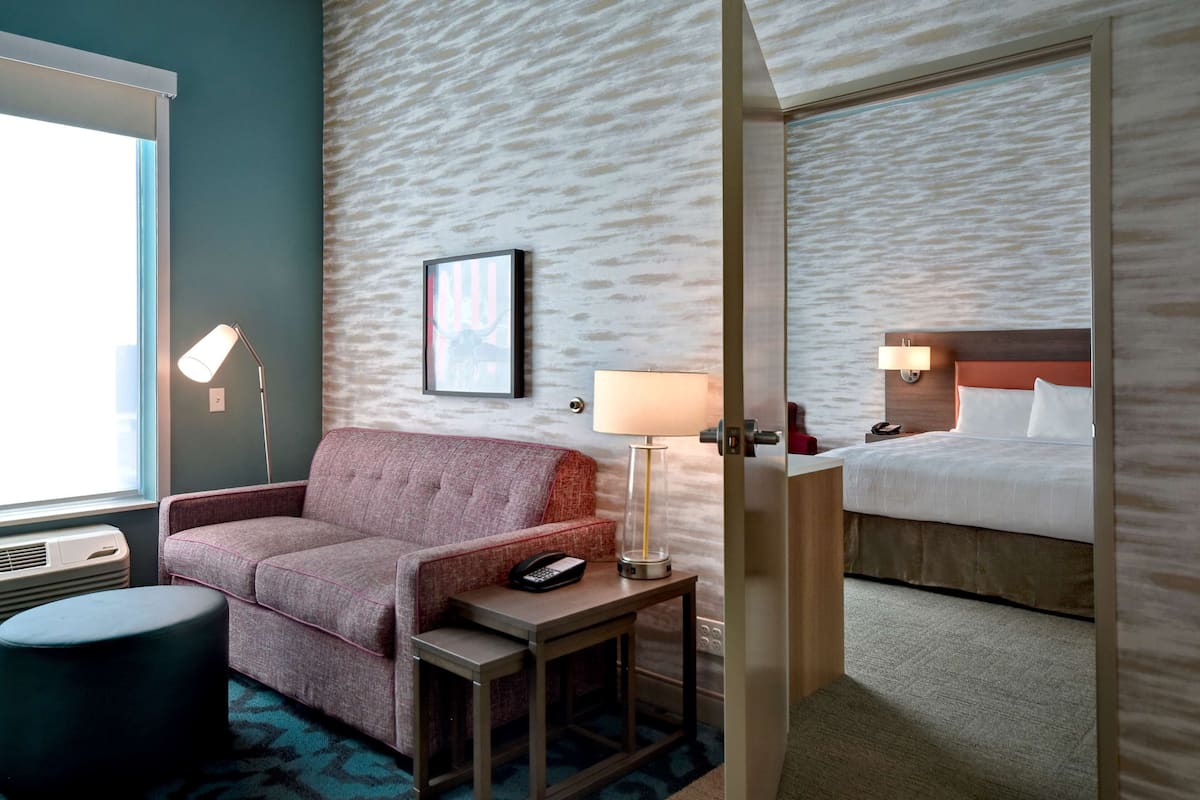 A hotel room with a sofa, a bedside table with a lamp, a bed, and a wall-mounted telephone.