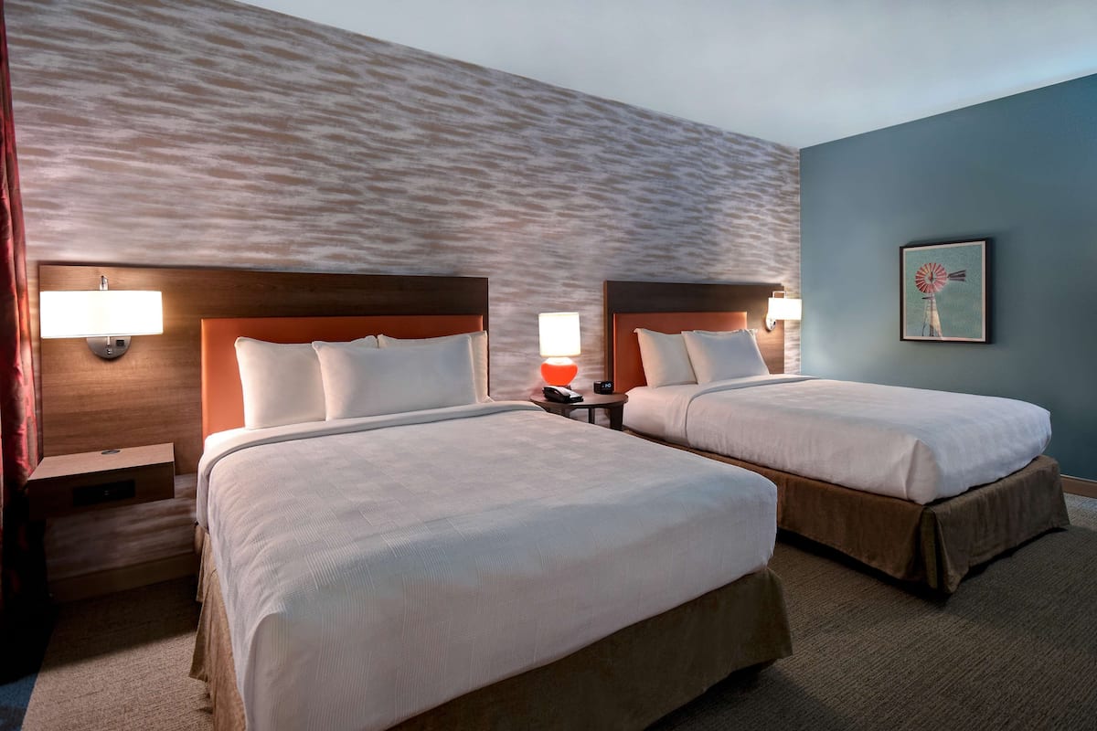 A hotel room with two beds, a nightstand with a lamp, and a wall with a textured pattern.