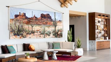 Uma sala de estar com uma grande pintura de paisagem desértica, um sofá com almofadas estampadas, uma mesa de centro e um armário de madeira com prateleiras.