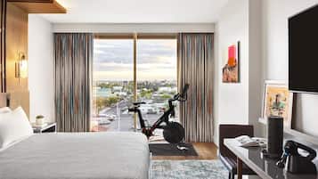 Quarto de hotel moderno com uma cama grande, uma escrivaninha, uma bicicleta e vista para a cidade.