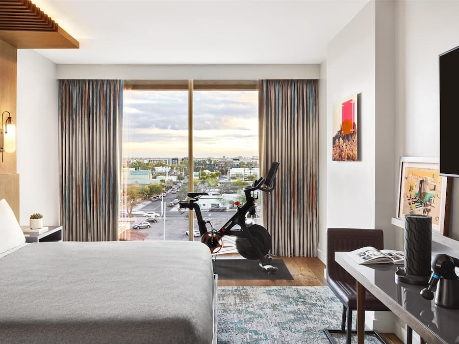 Quarto de hotel moderno com uma cama grande, uma escrivaninha, uma bicicleta e vista para a cidade.