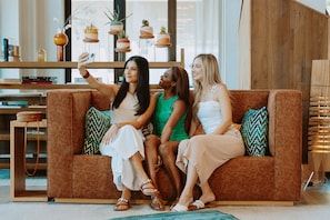 A modern living room with a brown sofa, decorative plants, and a bookshelf. - Canopy by Hilton Scottsdale Old Town (Scottsdale)