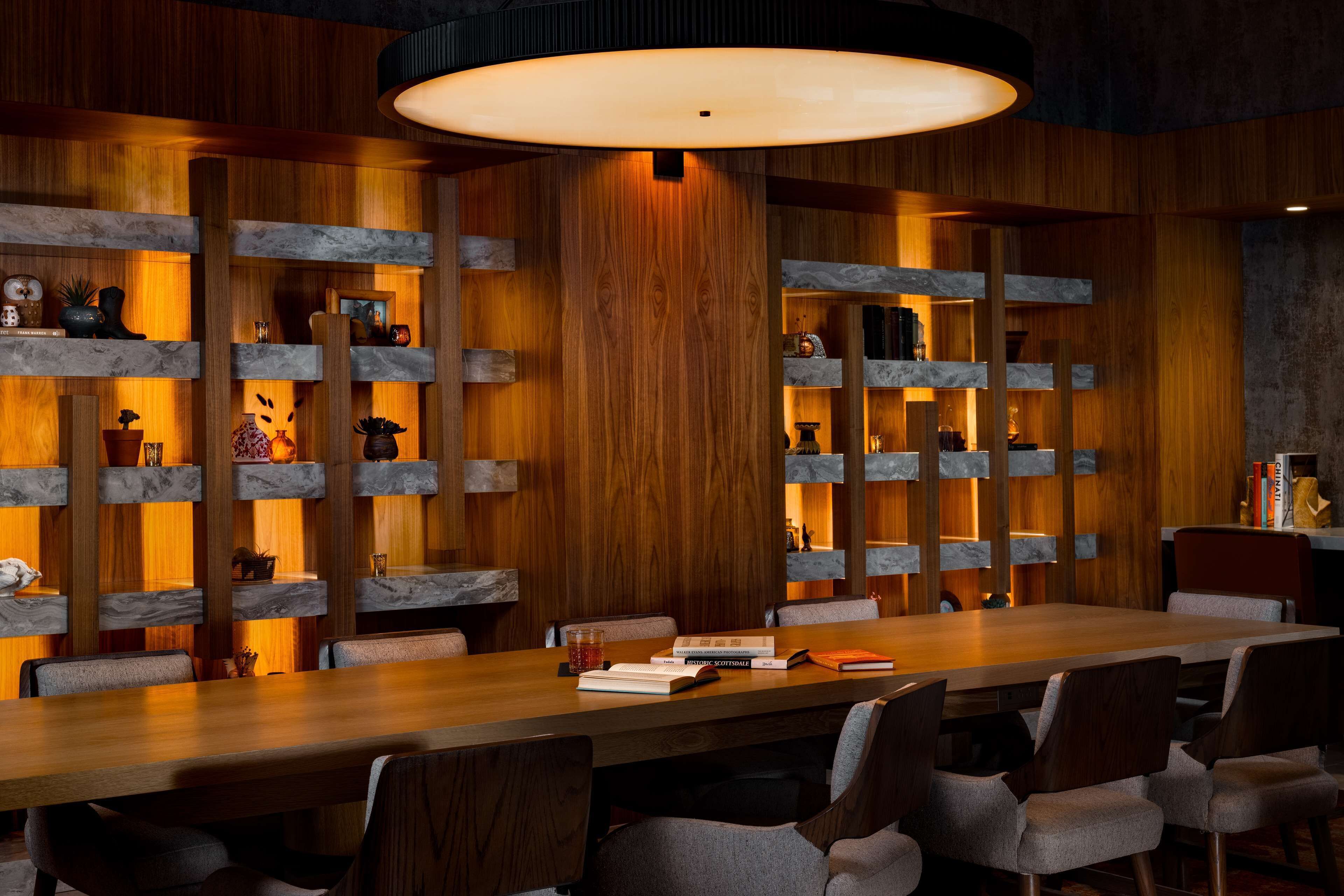 A conference room with a long table, multiple chairs, and shelves with various items.