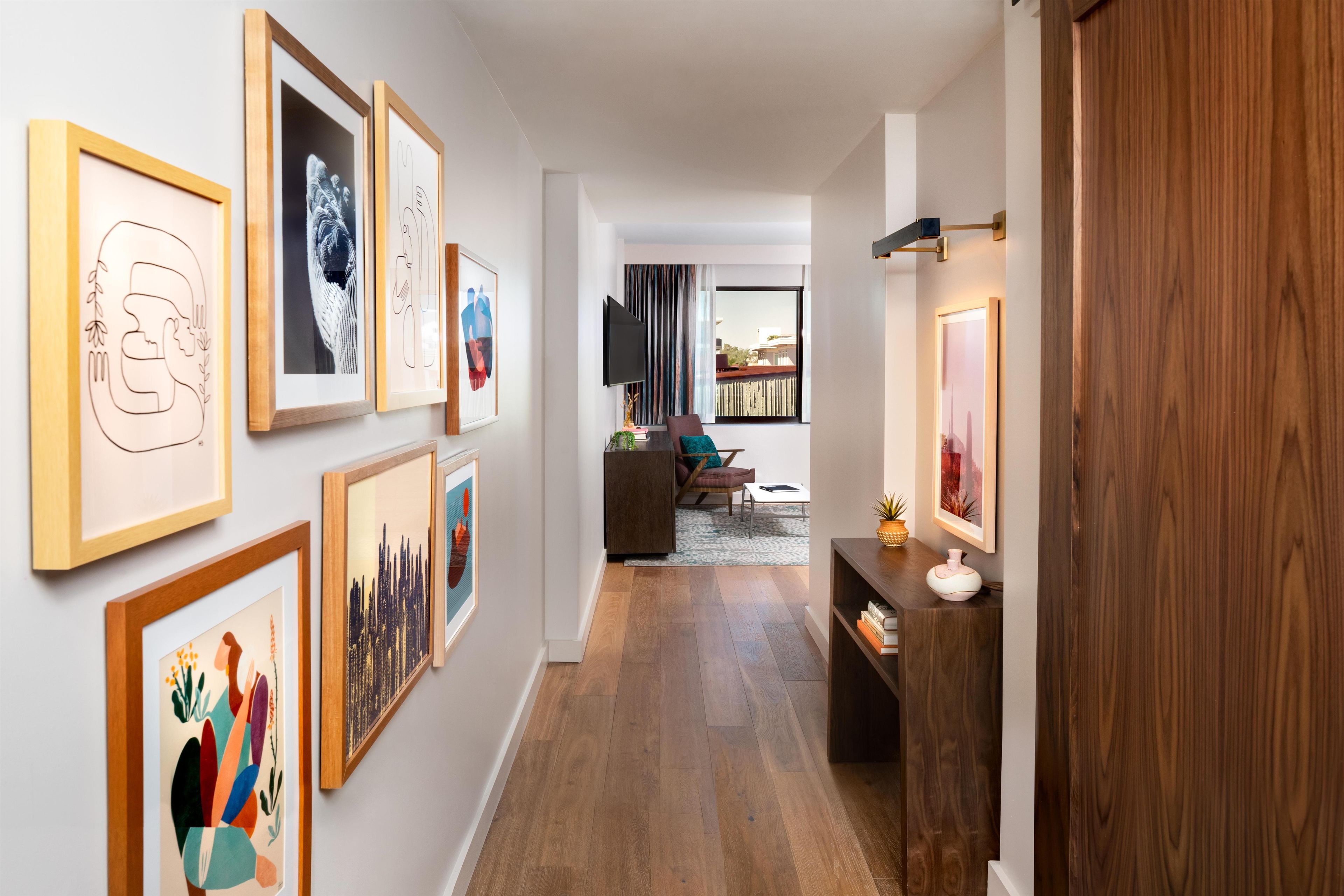 Un pasillo con obras enmarcadas en las paredes, piso de madera y vista a una sala de estar con sofá y televisor.