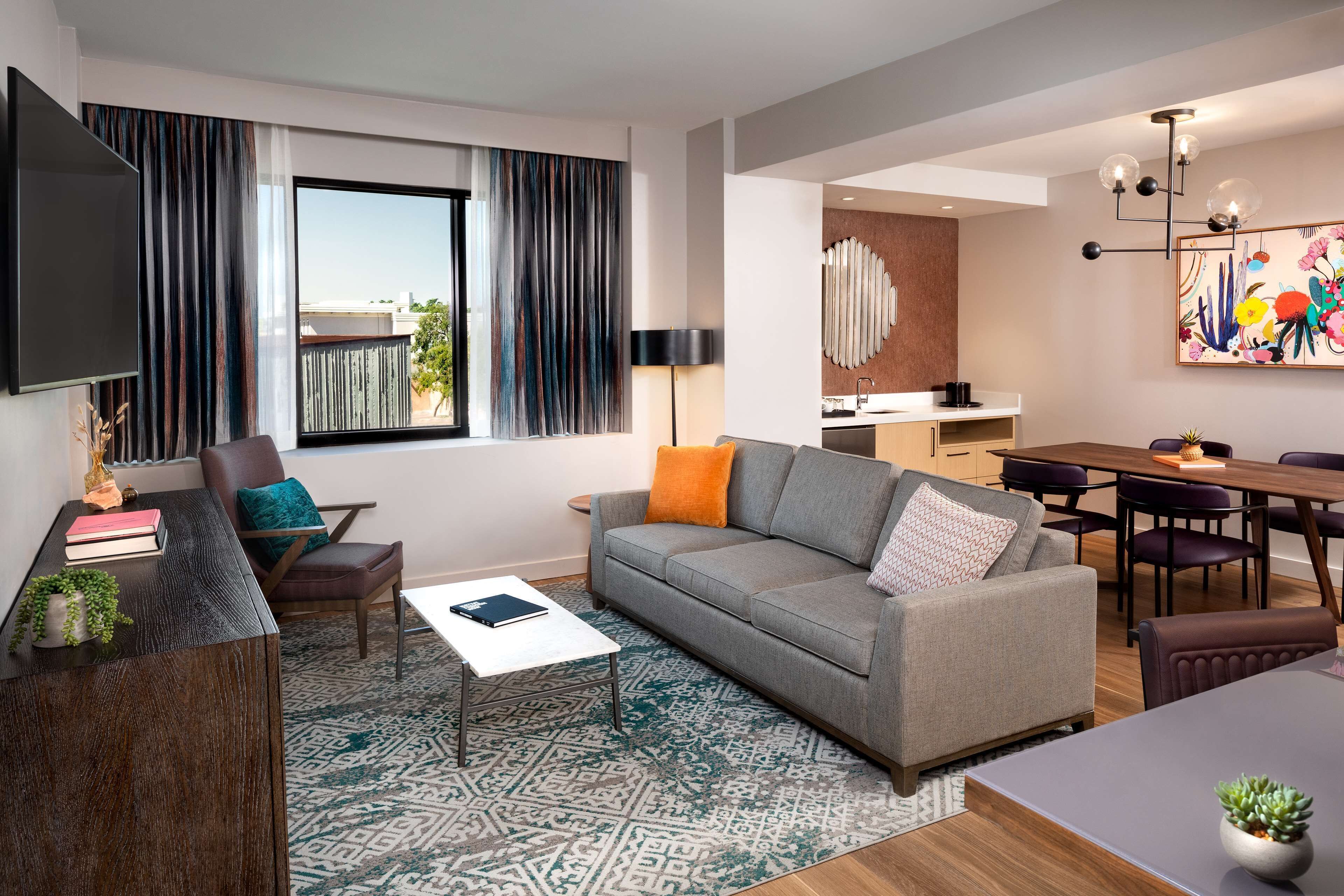 Uma sala de estar moderna com um sofá cinzento, uma mesa de centro, uma televisão e um espaço de jantar com mesa e cadeiras.