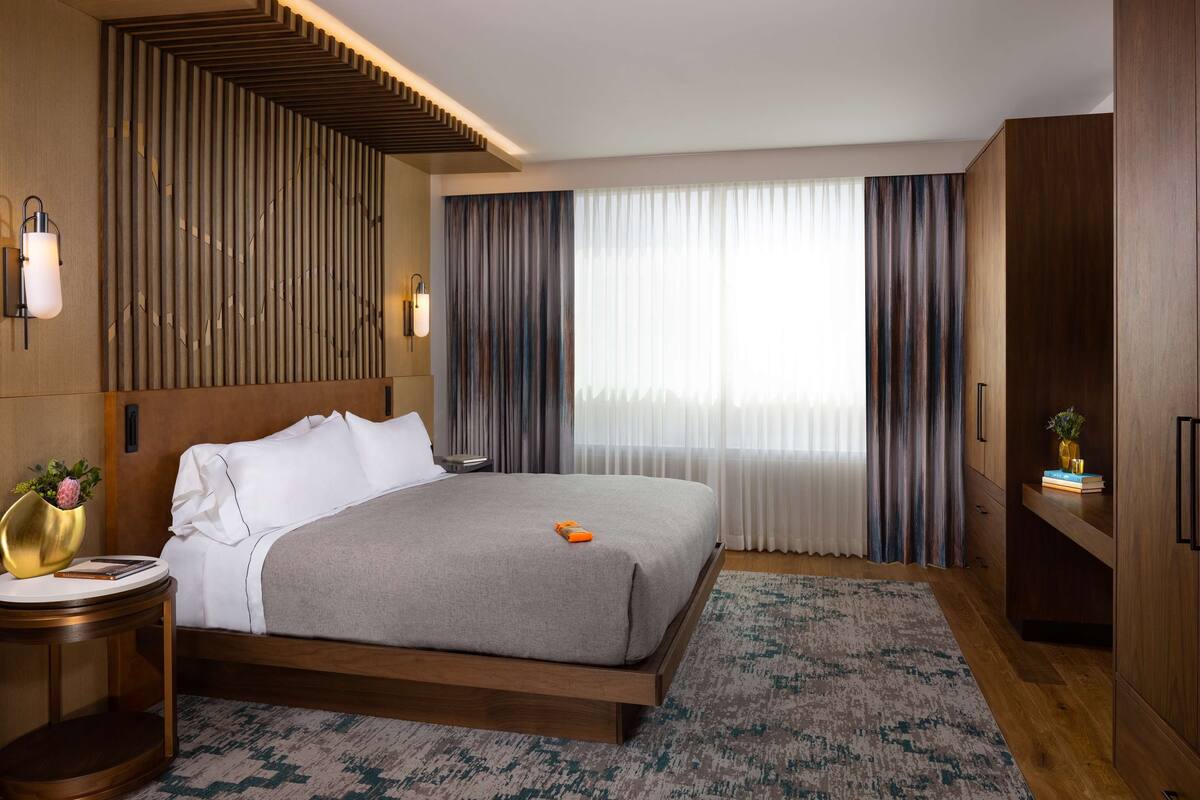 Habitación de hotel moderna con una cama grande, una mesita de noche, un armario y un ventanal con cortinas.