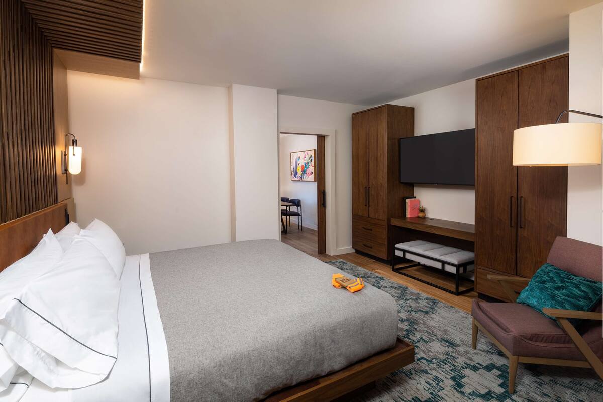 Una habitación de hotel moderna con una cama grande, un escritorio, una silla, un televisor y un armario.