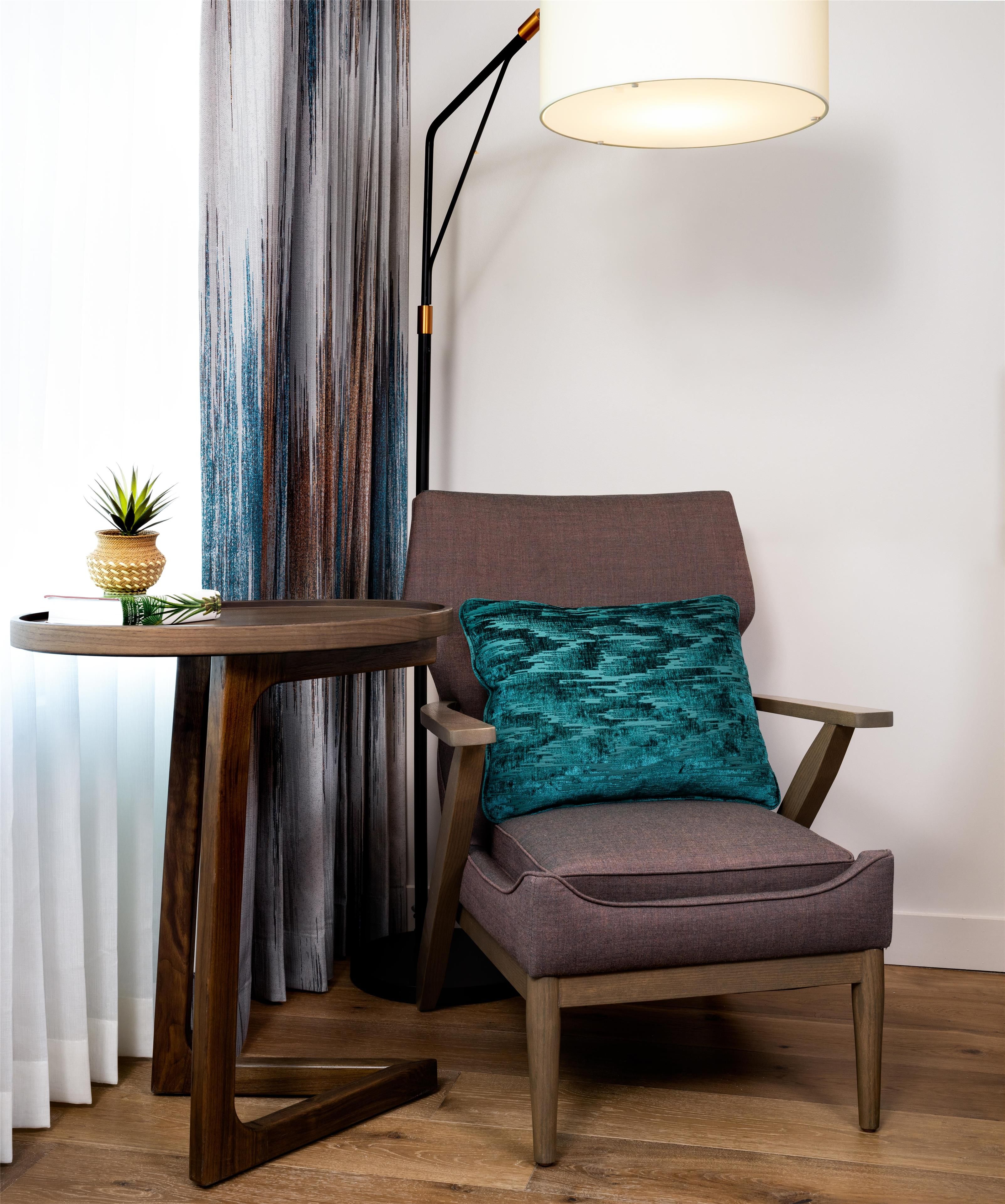 A modern armchair with a textured cushion, a round wooden side table with a small plant, and a floor lamp with a white shade.