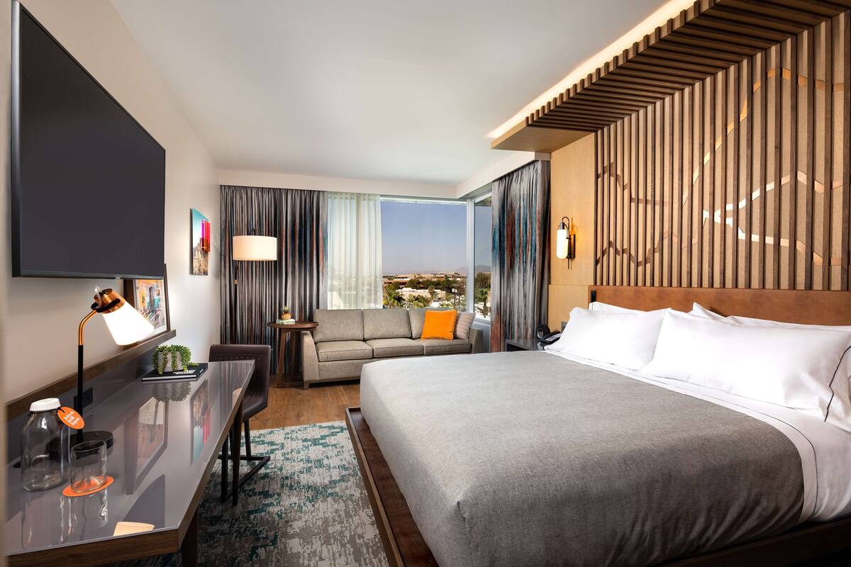 Una habitación de hotel moderna con una cama grande, un escritorio con lámpara, un sofá y vistas a la ciudad.