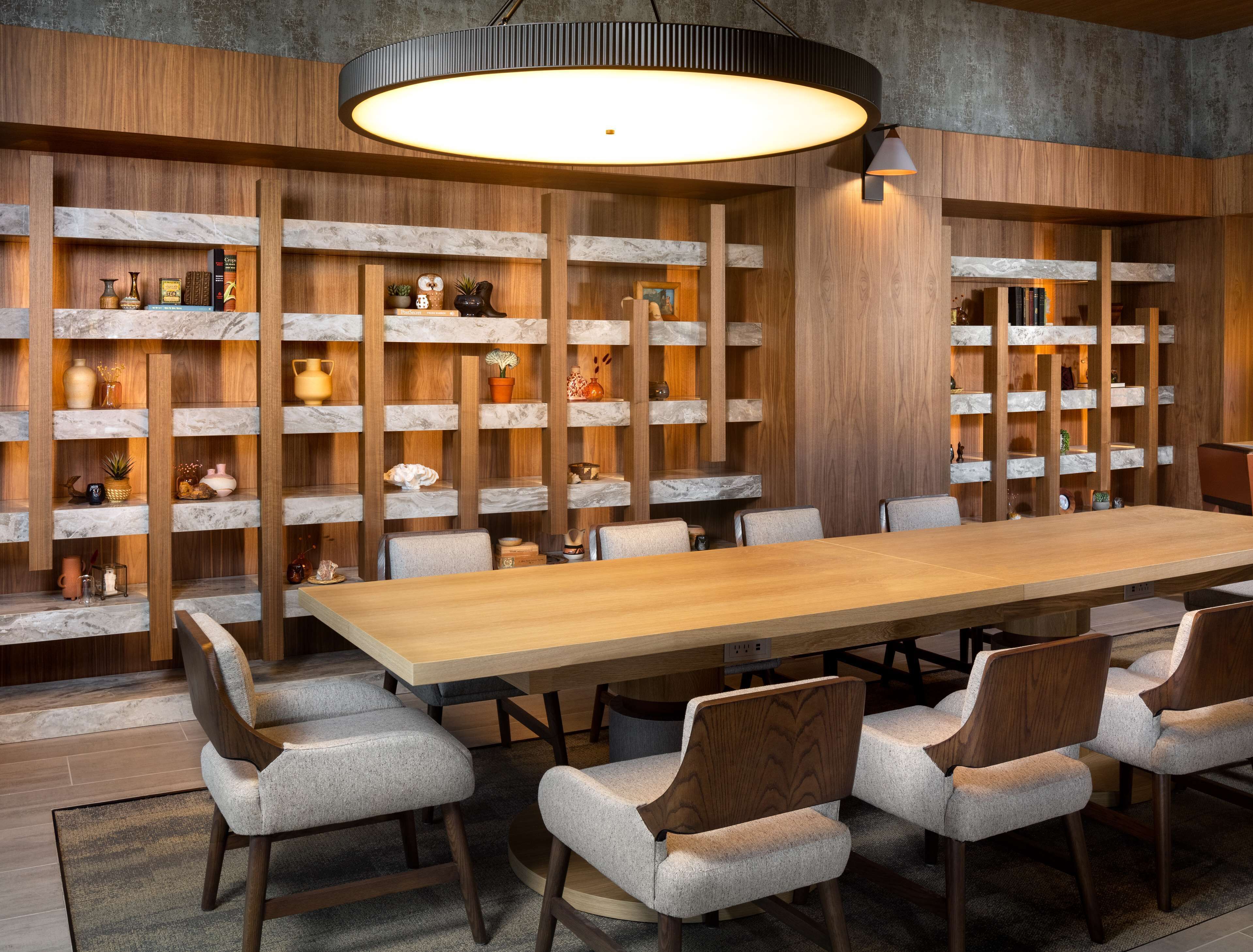 Un'elegante zona pranzo con un lungo tavolo in legno, sei sedie imbottite ed scaffali in marmo con diversi oggetti decorativi.