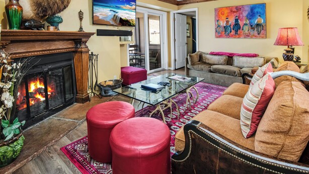 A living room with a fireplace, a glass coffee table, red ottomans, a sofa, and a painting on the wall. - Platinum Luxury Condo in Heart of Avon A606 (Avon)