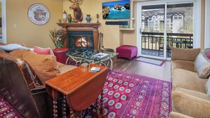 A cozy living room with a fireplace, a television, and a balcony with a view of buildings. - Platinum Luxury Condo in Heart of Avon A606 (Avon)
