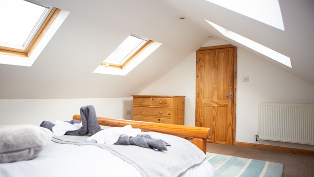Une chambre avec un plafond en pente, des fenêtres de toit, une armoire en bois, un radiateur et un lit recouvert d’un tapis à rayures.