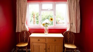 Une pièce avec une fenêtre, deux chaises, une table en bois et un vase rempli de fleurs.