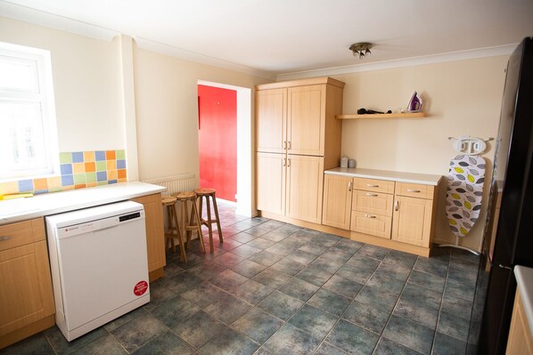 Una cocina compacta con lavavajillas, armarios de madera, una puerta roja y suelo de baldosas.
