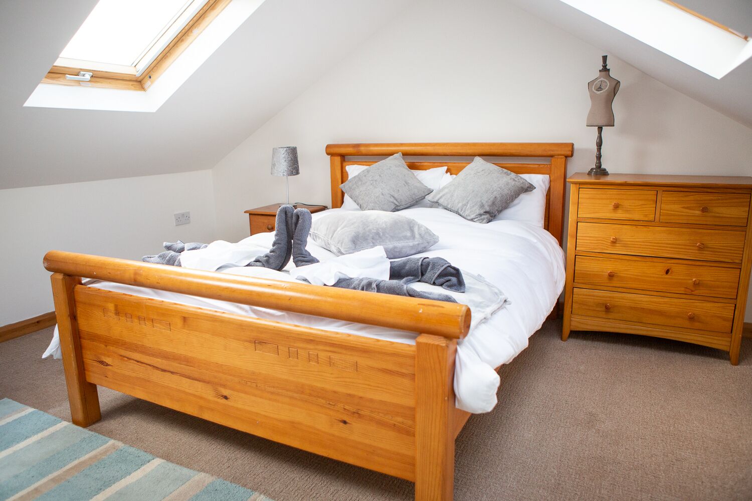 A bedroom with a sloped ceiling, a wooden bed with a headboard, a nightstand, a dresser, and a lamp.