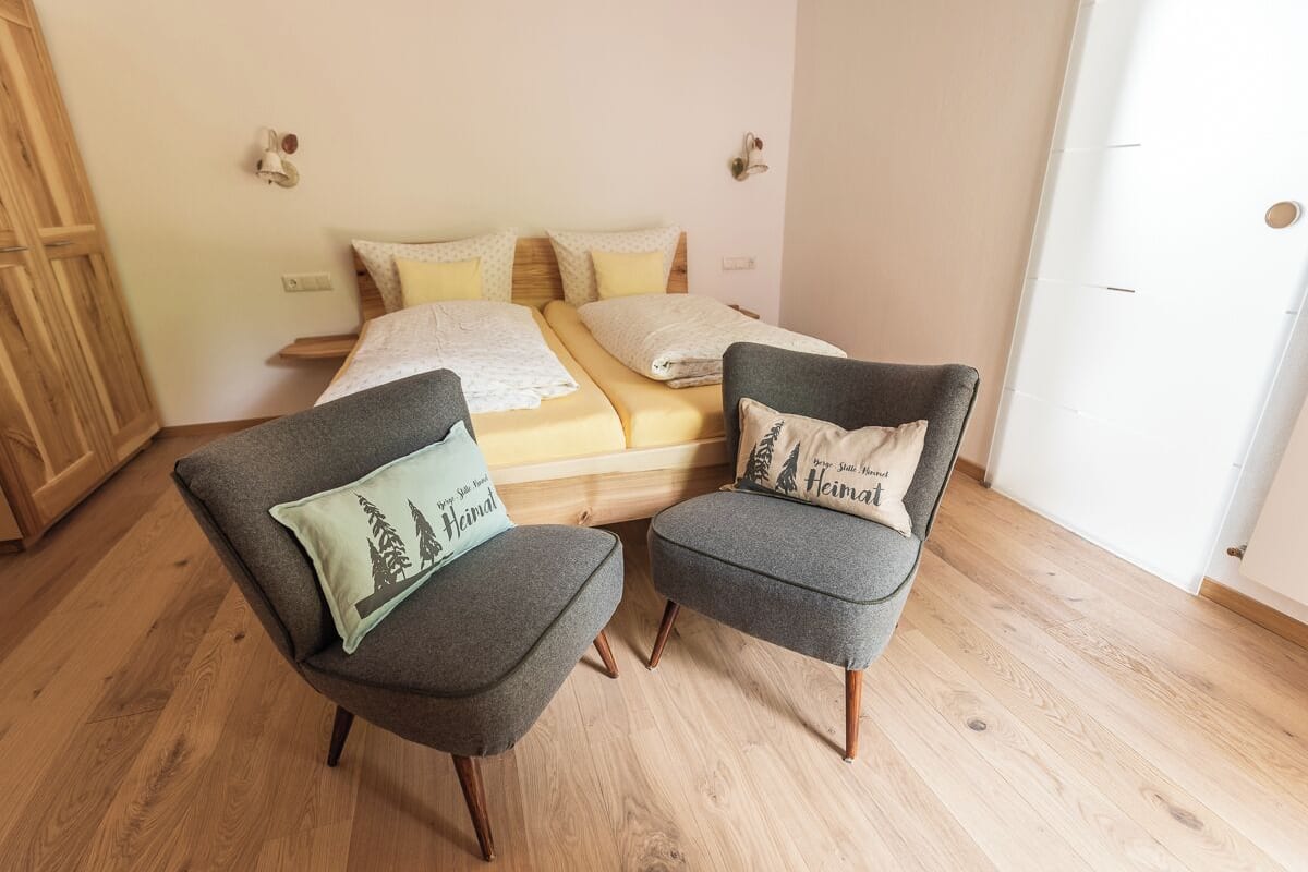 A bedroom with a bed, two grey armchairs, and a wooden wardrobe.
