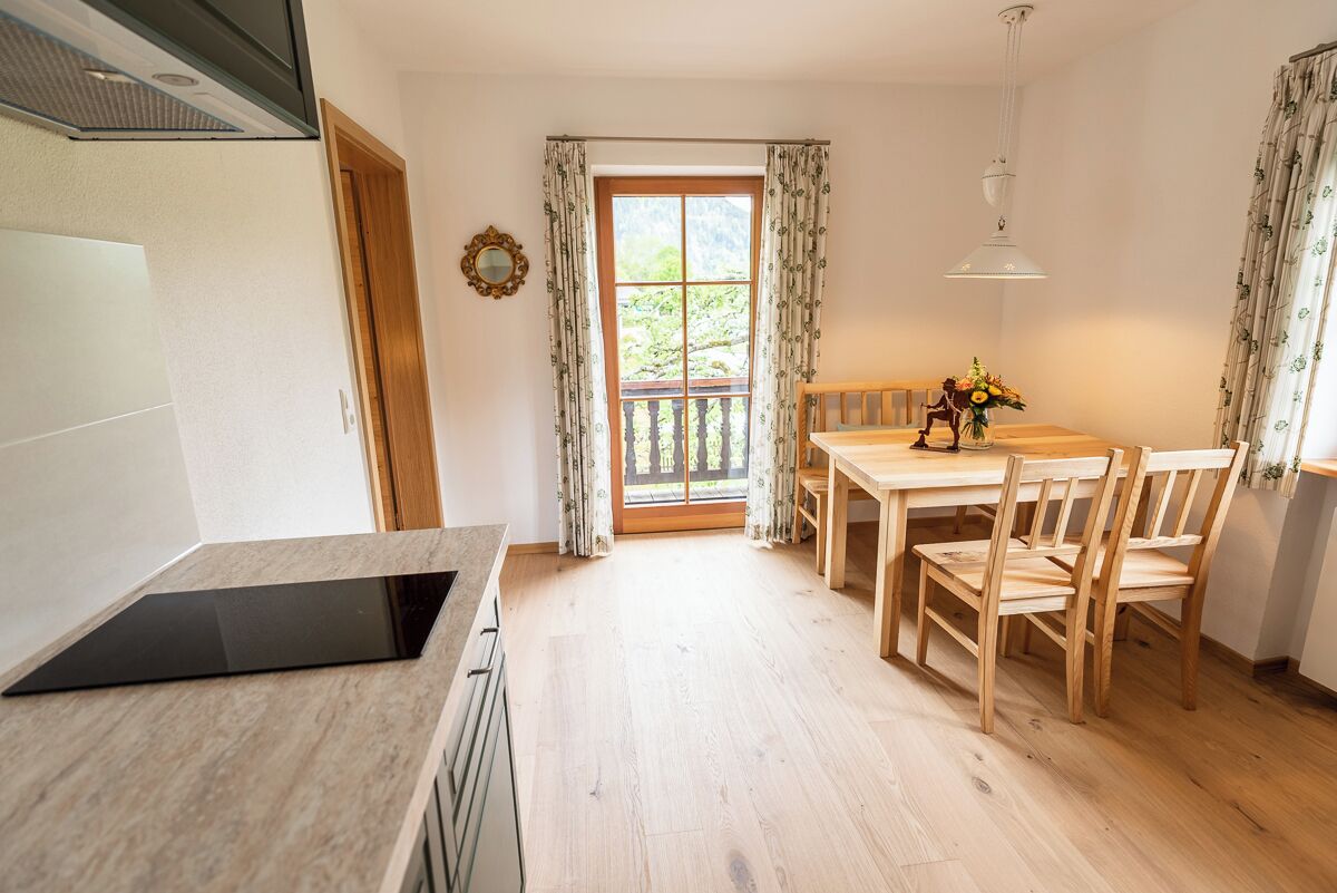 A kitchen with a dining area, a window with curtains, and a view of greenery outside.