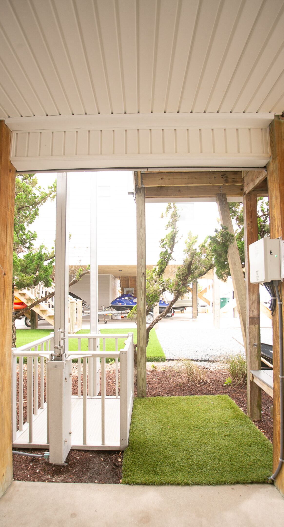 A covered outdoor area with a white railing, a small patch of artificial grass, and a wooden structure.