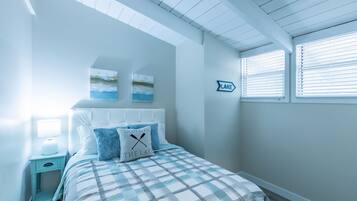 A bedroom with a bed, a nightstand, a wall-mounted lamp, a window with blinds, and a wall sign that says "LAKE".