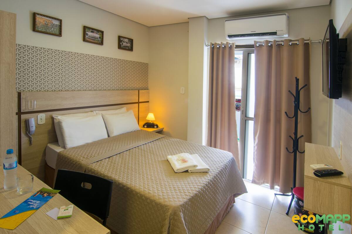 Ein Hotelzimmer mit Bett, Nachttisch, Lampe und Fernseher an der Wand.
