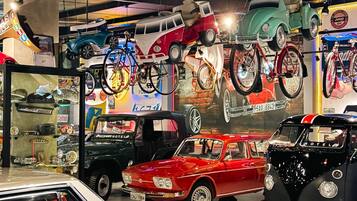 A vintage car showroom with various classic cars on display, including a red VW Beetle and a black VW van.