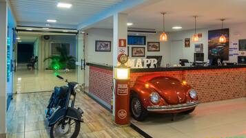 Un vestíbulo de hotel con un coche antiguo, una motocicleta y un mostrador de recepción.