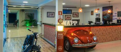 A hotel lobby with a vintage car, a motorcycle, and a reception desk.