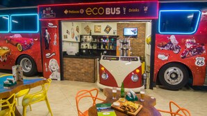 Eine busförmige Bar mit einem Oldtimer-VW-Bus als Blickfang, Tische mit Stühlen und einer Bar mit Flaschen und einem Bildschirm.
