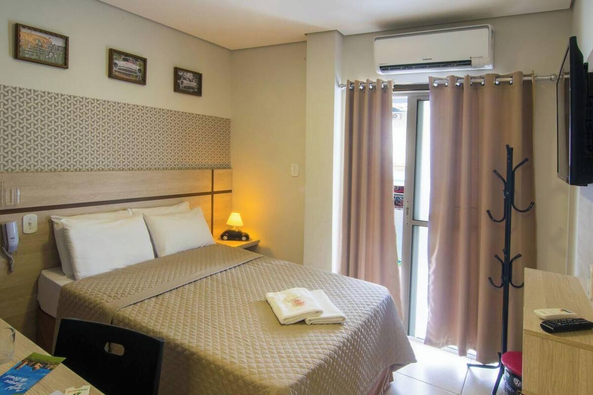 Ein Hotelzimmer mit Bett, Nachttisch, Lampe und einem an der Wand befestigten Fernseher.