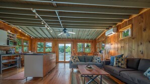 A spacious living area with a wooden ceiling, a sofa, a coffee table, and a kitchen area with a refrigerator and microwave.