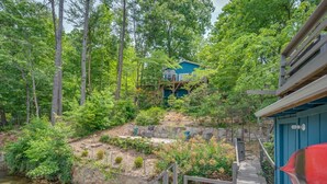 A cabin surrounded by dense forest, with a wooden deck leading to the entrance.