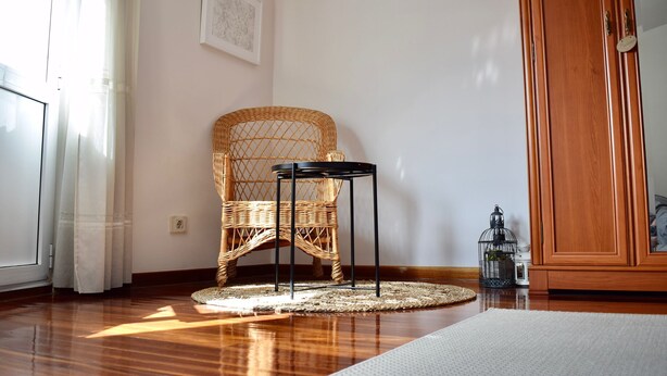 Una habitación con una silla de mimbre, una mesita, un armario de madera y un farol en el suelo.