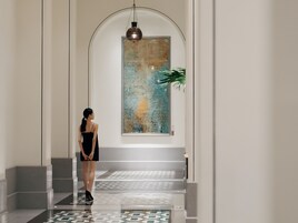 Una mujer con un vestido negro parada en un pasillo con piso estampado, un cuadro abstracto de gran tamaño en la pared y una lámpara colgante.