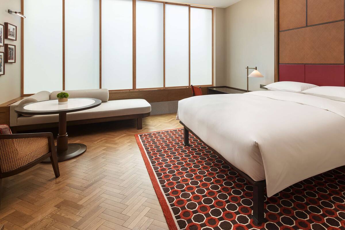 A hotel room with a bed, a round table, a sofa, a chair, and a large window with a view.
